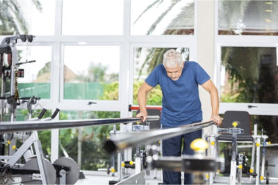 senior man taking support of bars while walking in fitness studio 